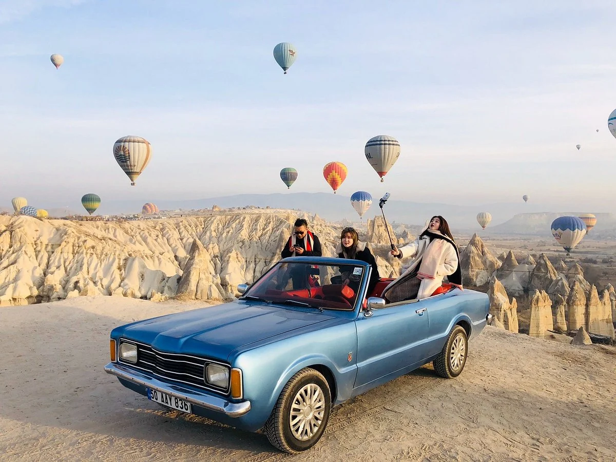 Friends riding in a blue classic convertible with balloons over Cappadocia