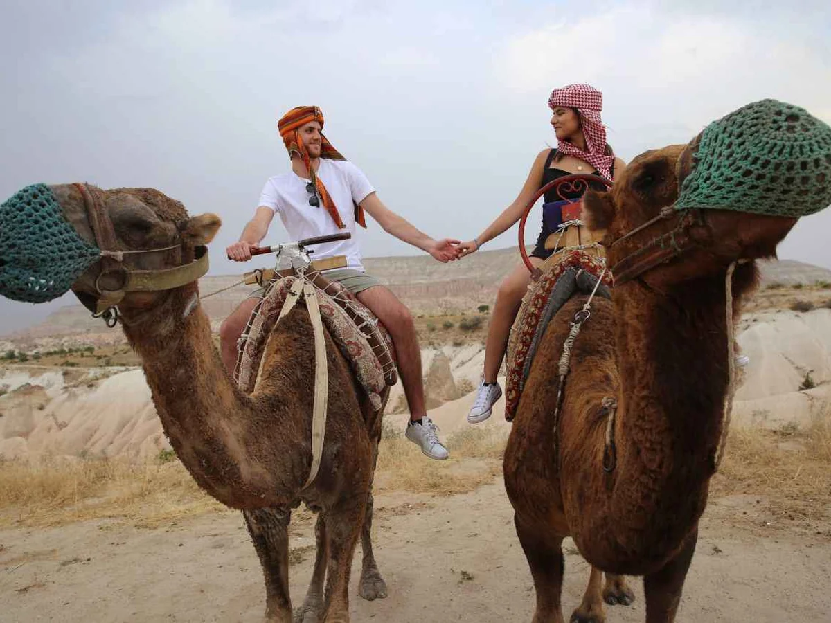 Couple holding hands while riding camels on a Cappadocia daytime tour