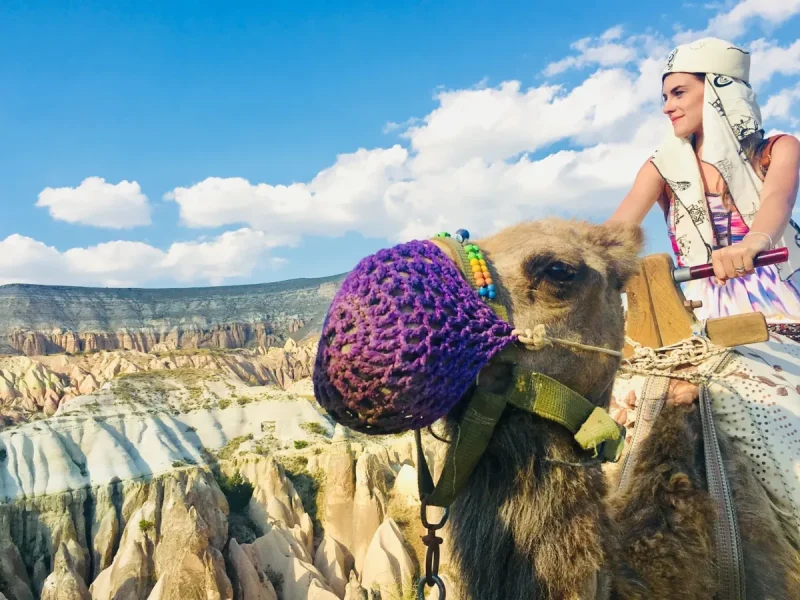 Traveler riding a decorated camel with Cappadocia valley views in daylight