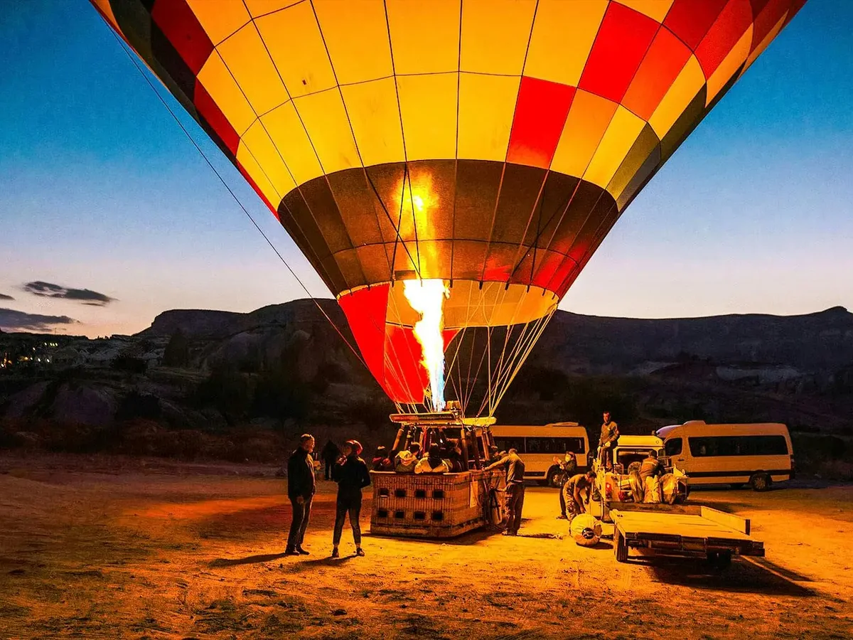 Balloon crew preparing a glowing hot air balloon for takeoff in Cat Valley