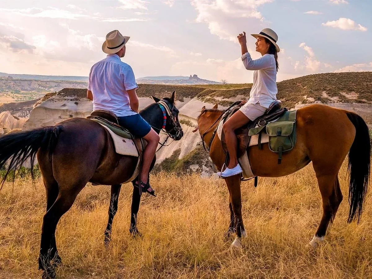 Two travelers enjoying a daytime horse riding tour across the Cappadocia landscape