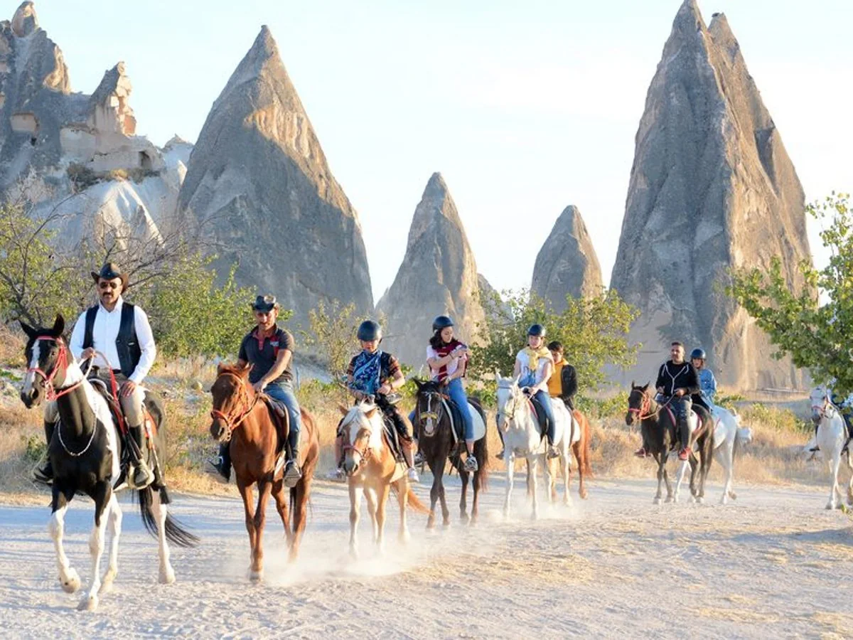Guided horseback riding group approaching tall fairy chimneys in Cappadocia