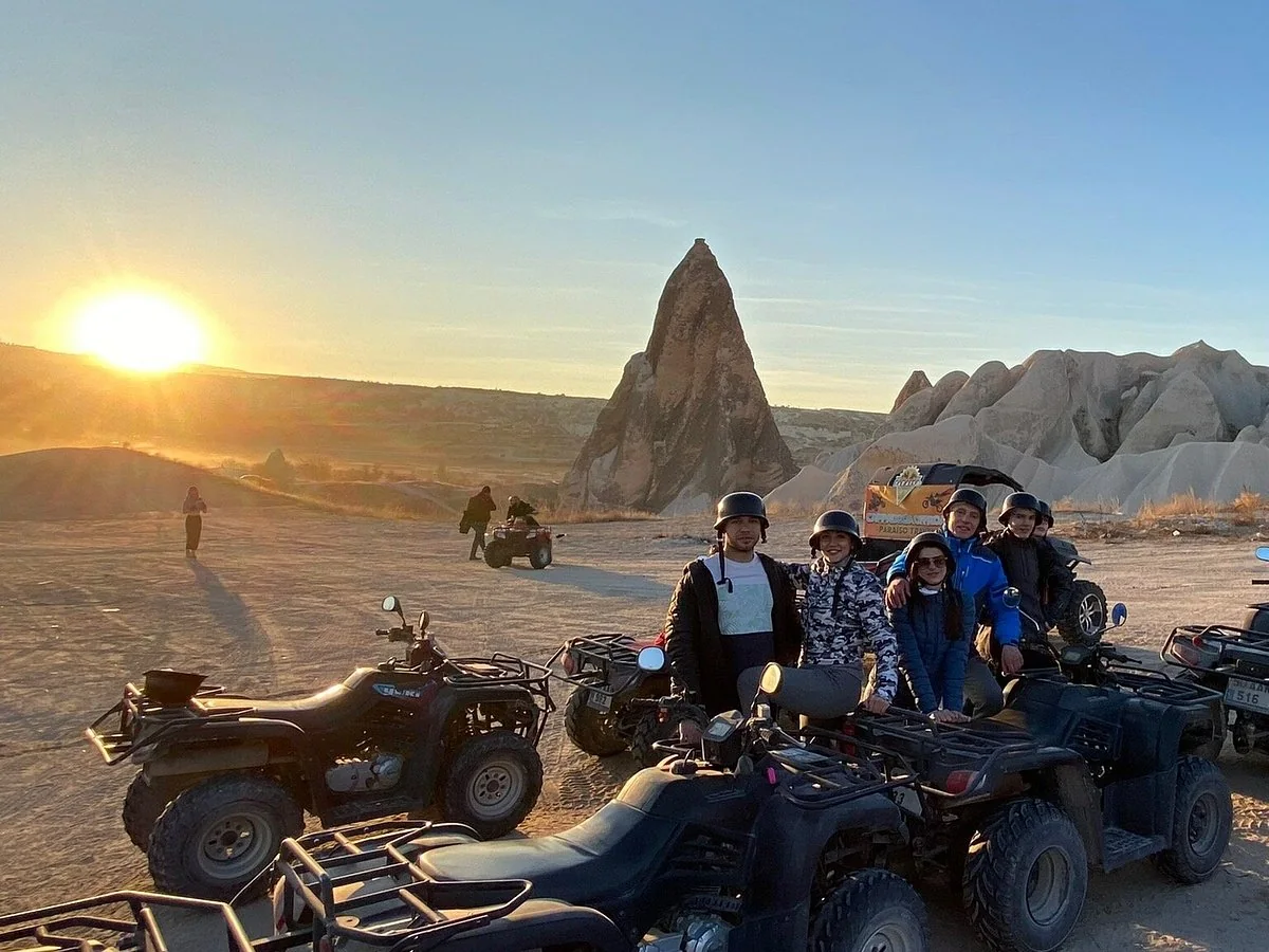 Friends posing with quad bikes beside Cappadocia fairy chimneys at sunset