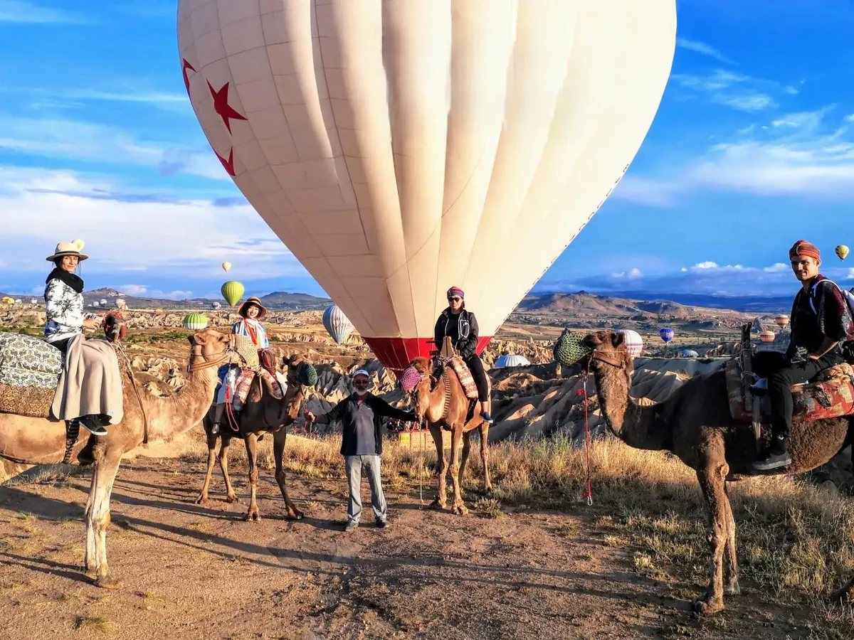Camel riders gathered beneath a large hot air balloon during a Cappadocia sunrise tour