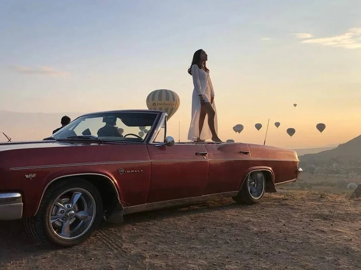 guest posing on a red classic convertible during a Cappadocia sunrise balloon tour