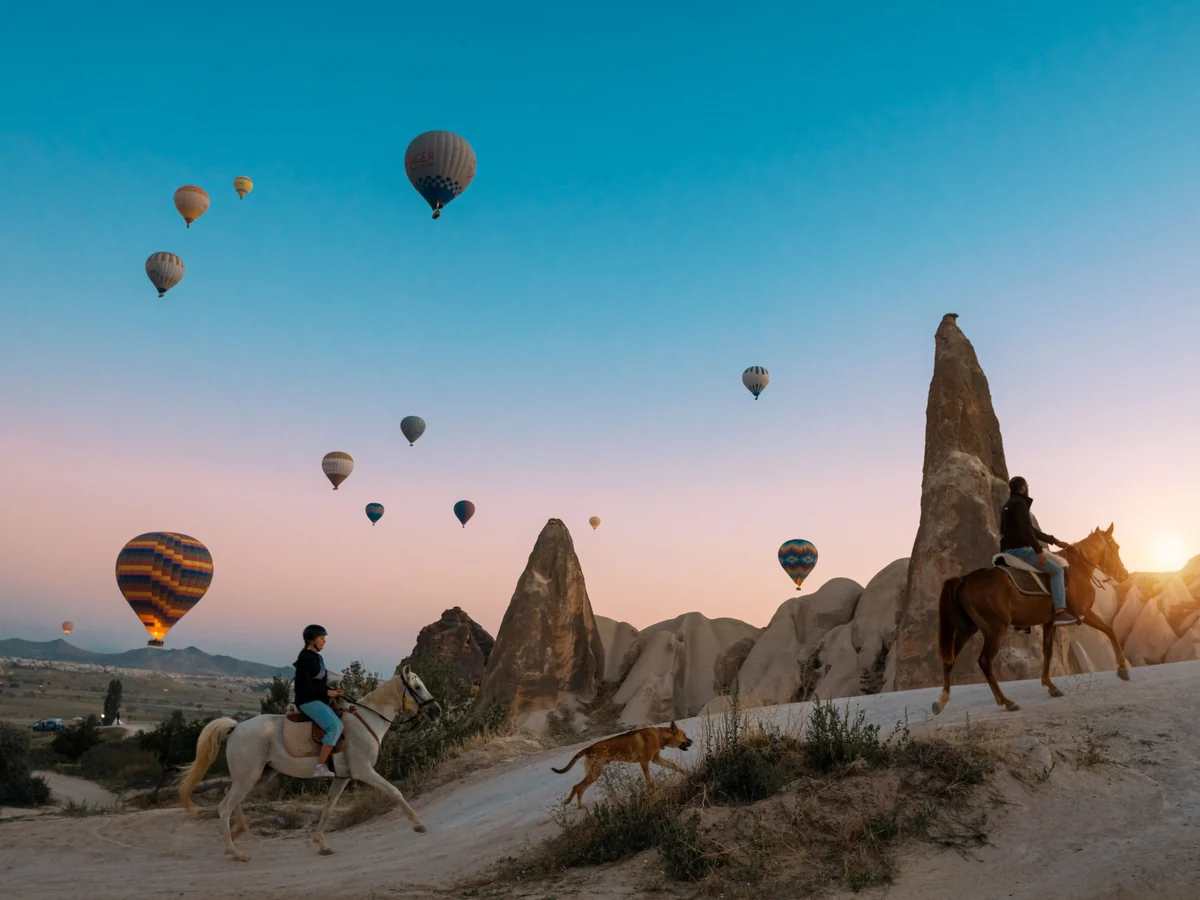 Guests riding horses through Cappadocia valleys during a colorful sunrise
