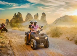 ATV riders crossing a dusty trail among Cappadocia fairy chimneys at sunset