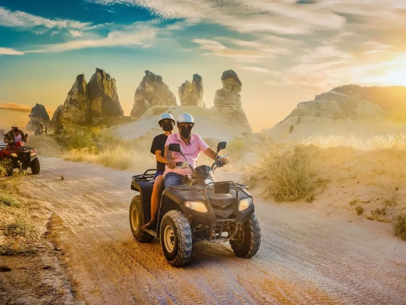 ATV riders crossing a dusty trail among Cappadocia fairy chimneys at sunset
