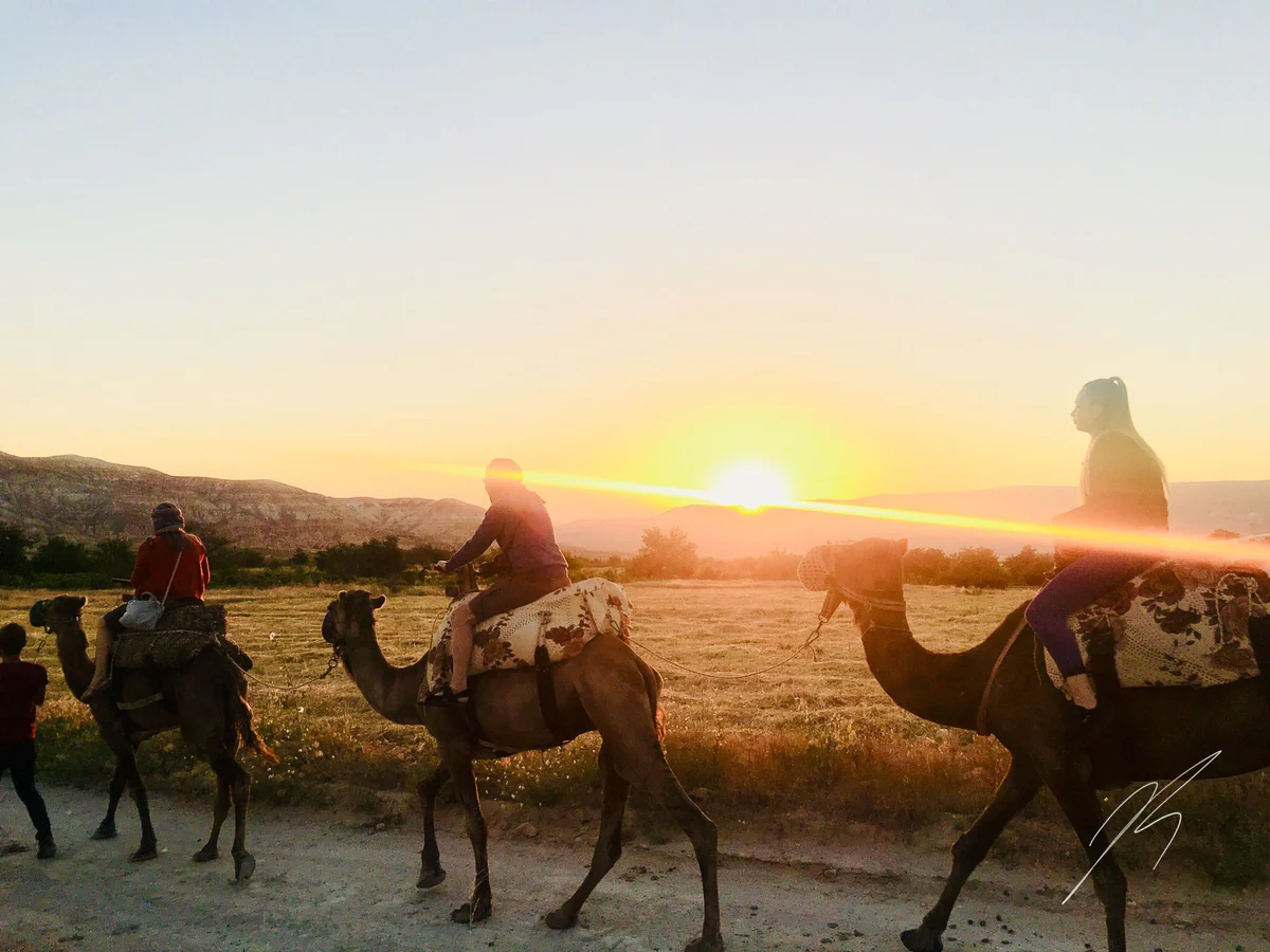 Camel riders crossing a Cappadocia valley during a glowing sunset
