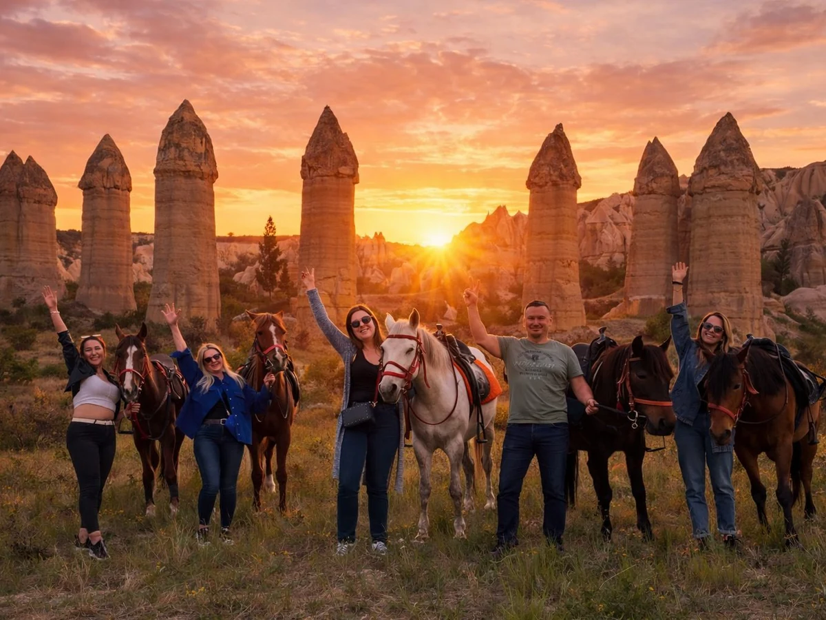 Group of riders posing with horses beside Cappadocia fairy chimneys at sunset