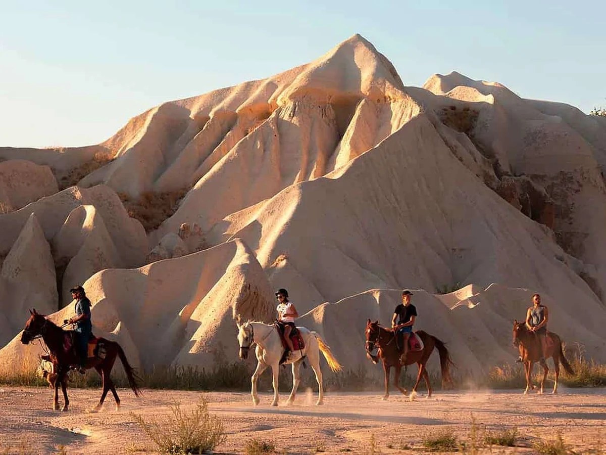 Horse riders crossing Cappadocia valleys during a sunset horse riding tour
