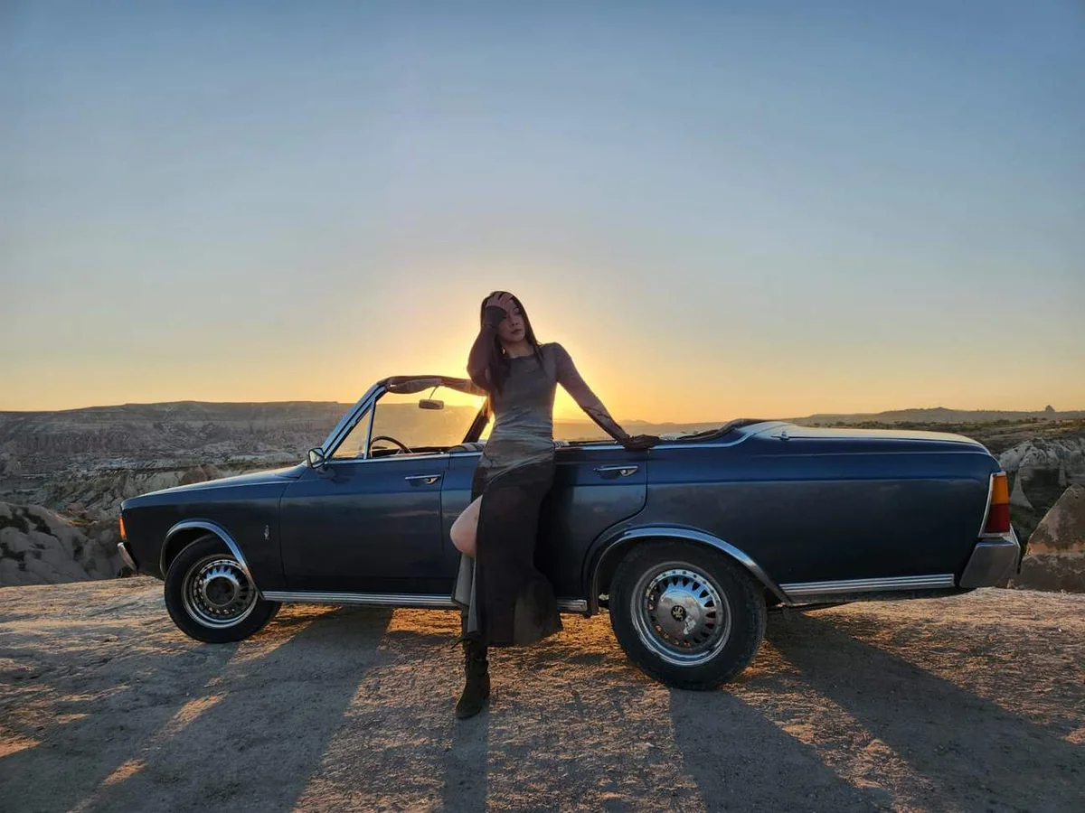 Woman posing beside a blue vintage car at sunset in Cappadocia