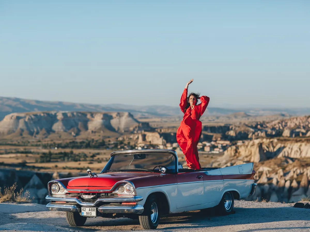 Woman standing in a vintage convertible overlooking Cappadocia at sunset