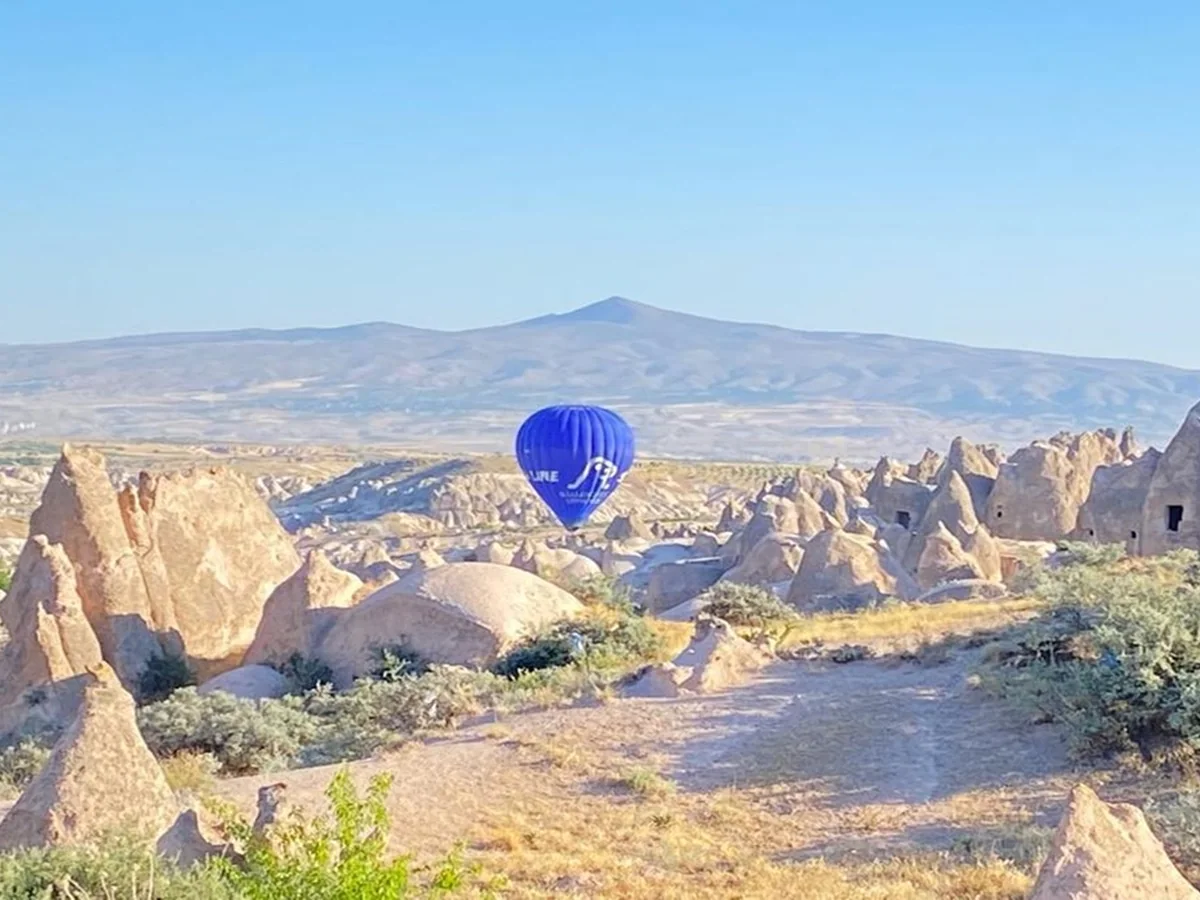Blue hot air balloon flying above the volcanic rock landscape of Cat Valley