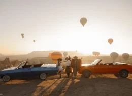 Blue and orange classic convertibles lined up during a Cappadocia balloon sunrise