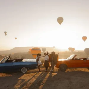 Blue and orange classic convertibles lined up during a Cappadocia balloon sunrise