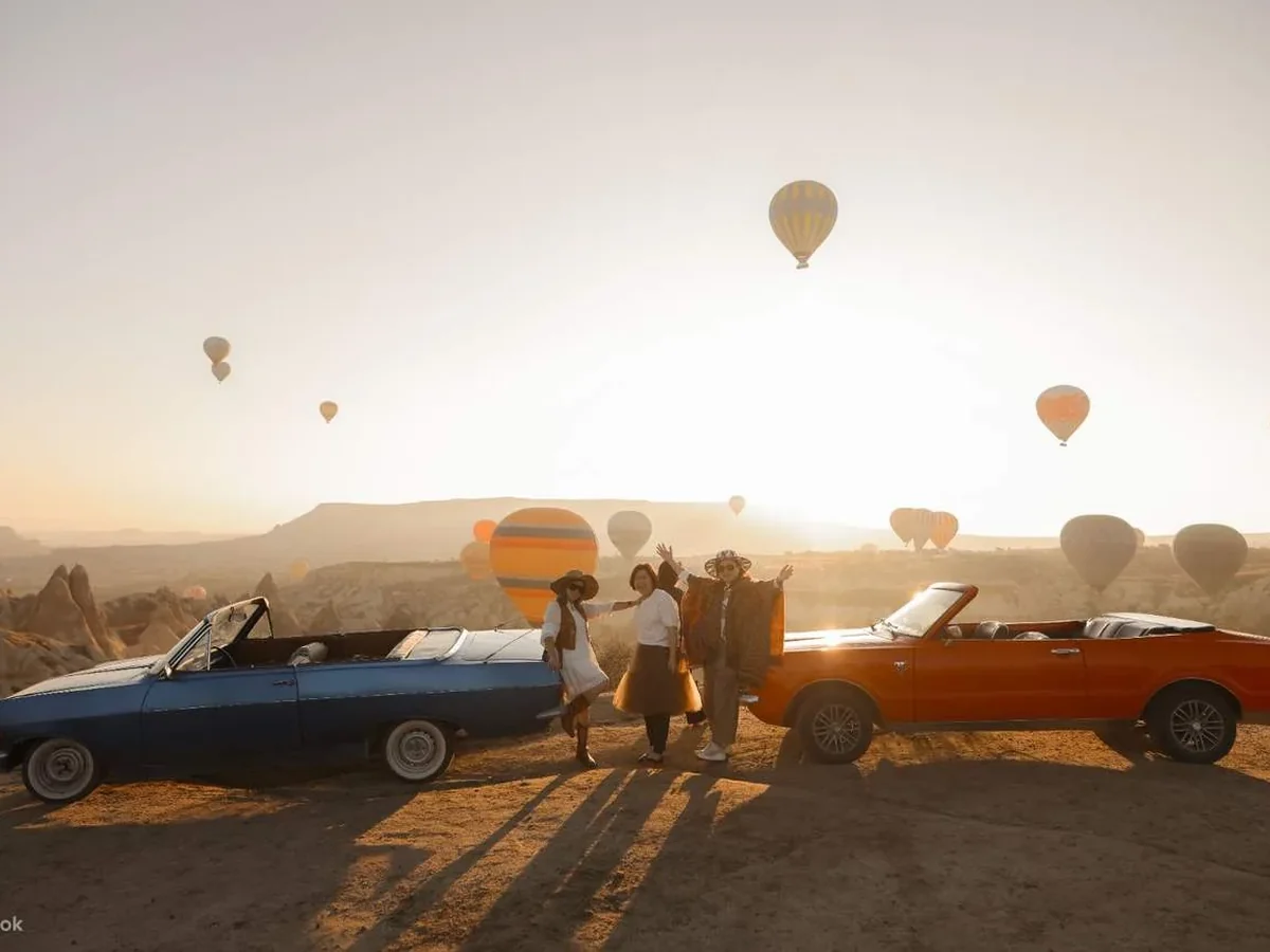 Blue and orange classic convertibles lined up during a Cappadocia balloon sunrise
