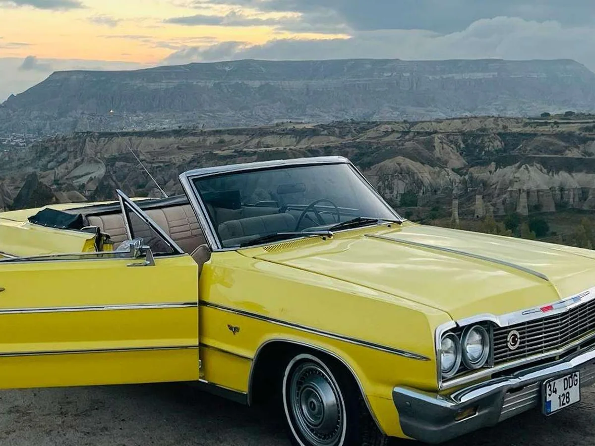 Yellow classic convertible parked above the Cappadocia valleys