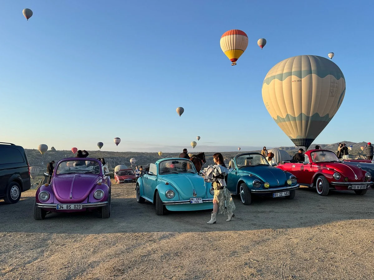 Colorful vintage cars gathered beneath hot air balloons at sunrise in Cappadocia