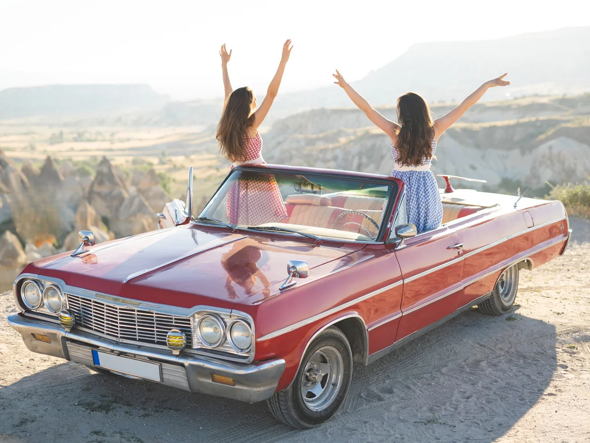 Two women enjoying the Cappadocia valley view from a red vintage convertible