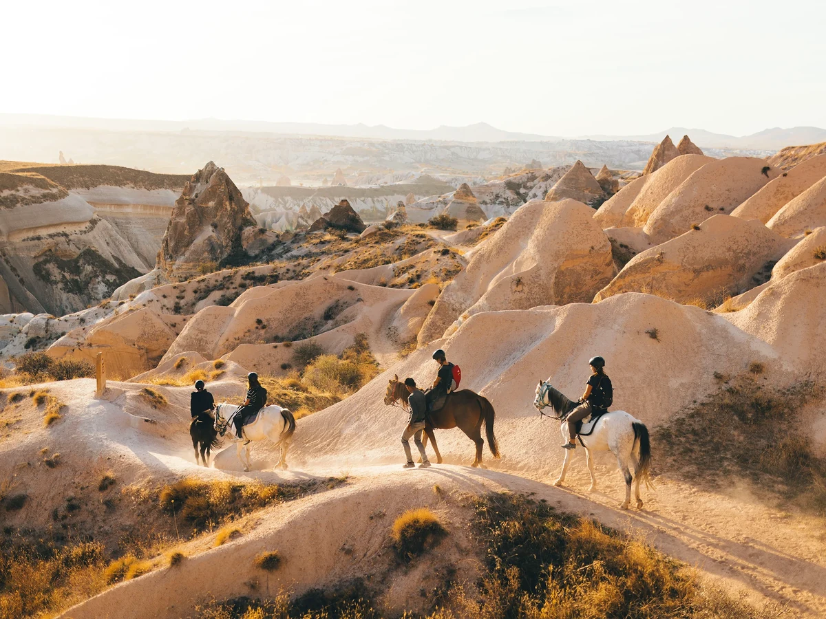 Horse riding group traveling among Göreme rock formations at sunset