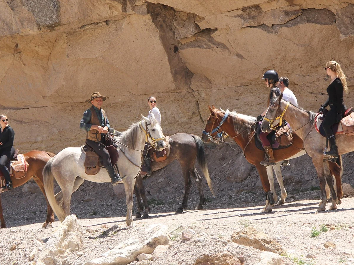 Guided horseback riding group passing beneath Cappadocia rock formations