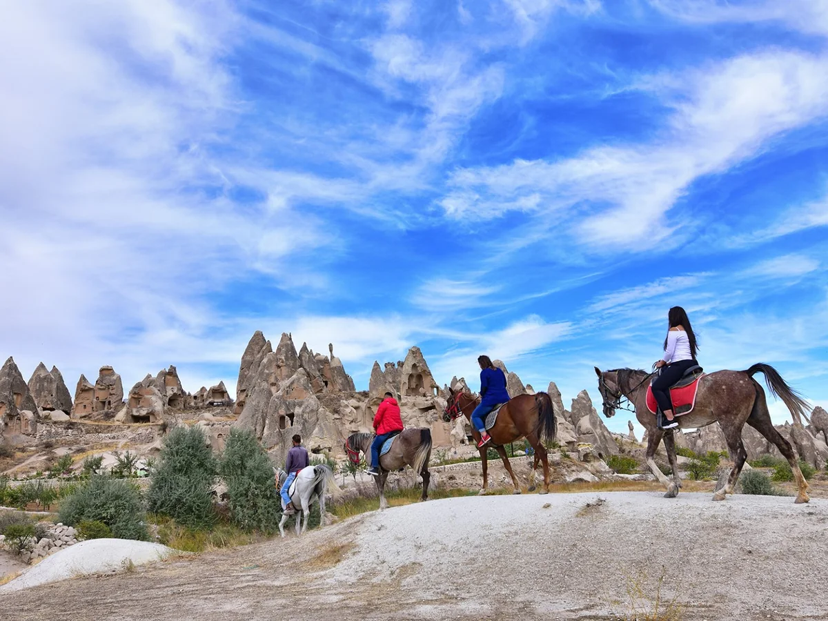 Horseback riders crossing a scenic trail beneath a blue Cappadocia sky