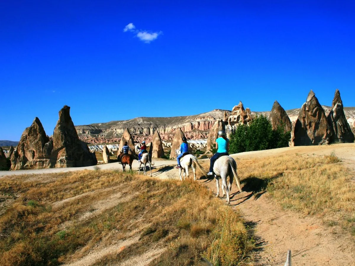 Horse riders exploring a wide Cappadocia valley surrounded by fairy chimneys