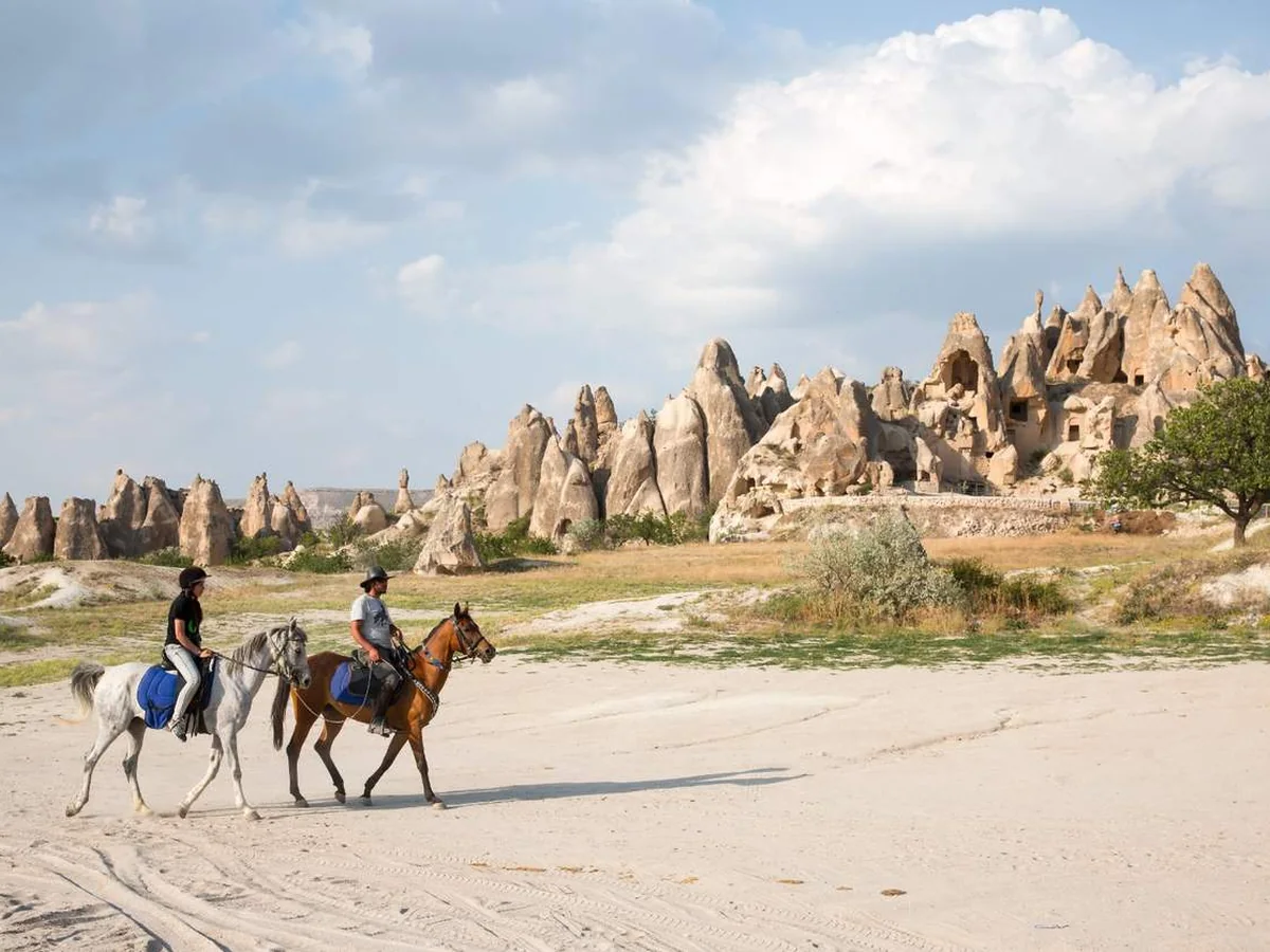Two horseback riders crossing an open Cappadocia valley with rock formations