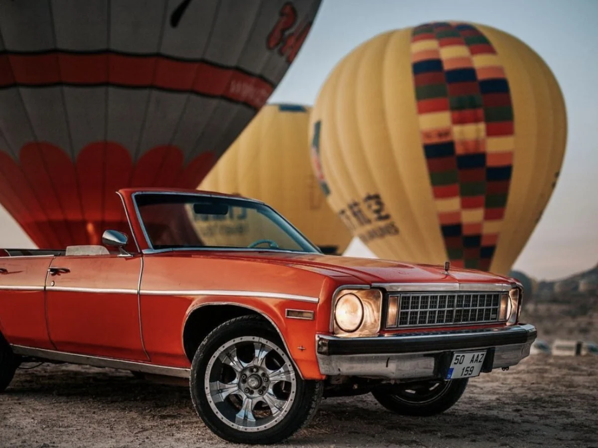 Orange classic convertible parked beside hot air balloons at sunrise in Cappadocia