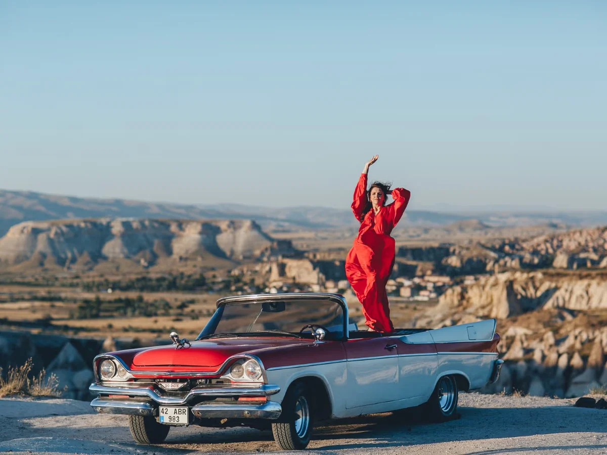 Woman posing on a red and blue vintage convertible overlooking the Cappadocia valleys