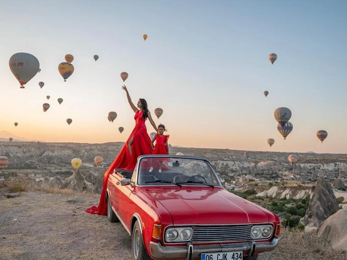 Woman in a red dress posing on a red vintage car at sunrise in Cappadocia
