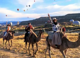 Camel riders enjoying sunrise balloon views along a scenic Cappadocia valley trail