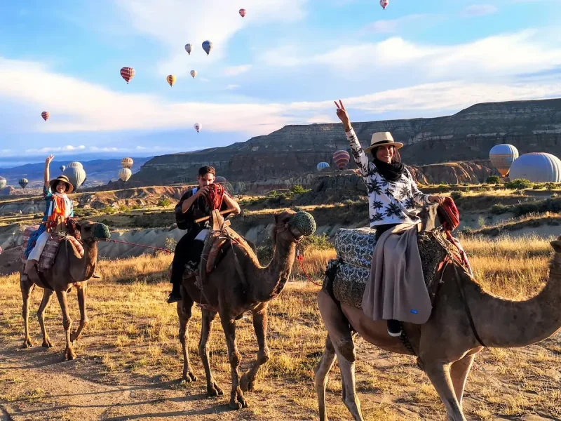 Camel riders enjoying sunrise balloon views along a scenic Cappadocia valley trail