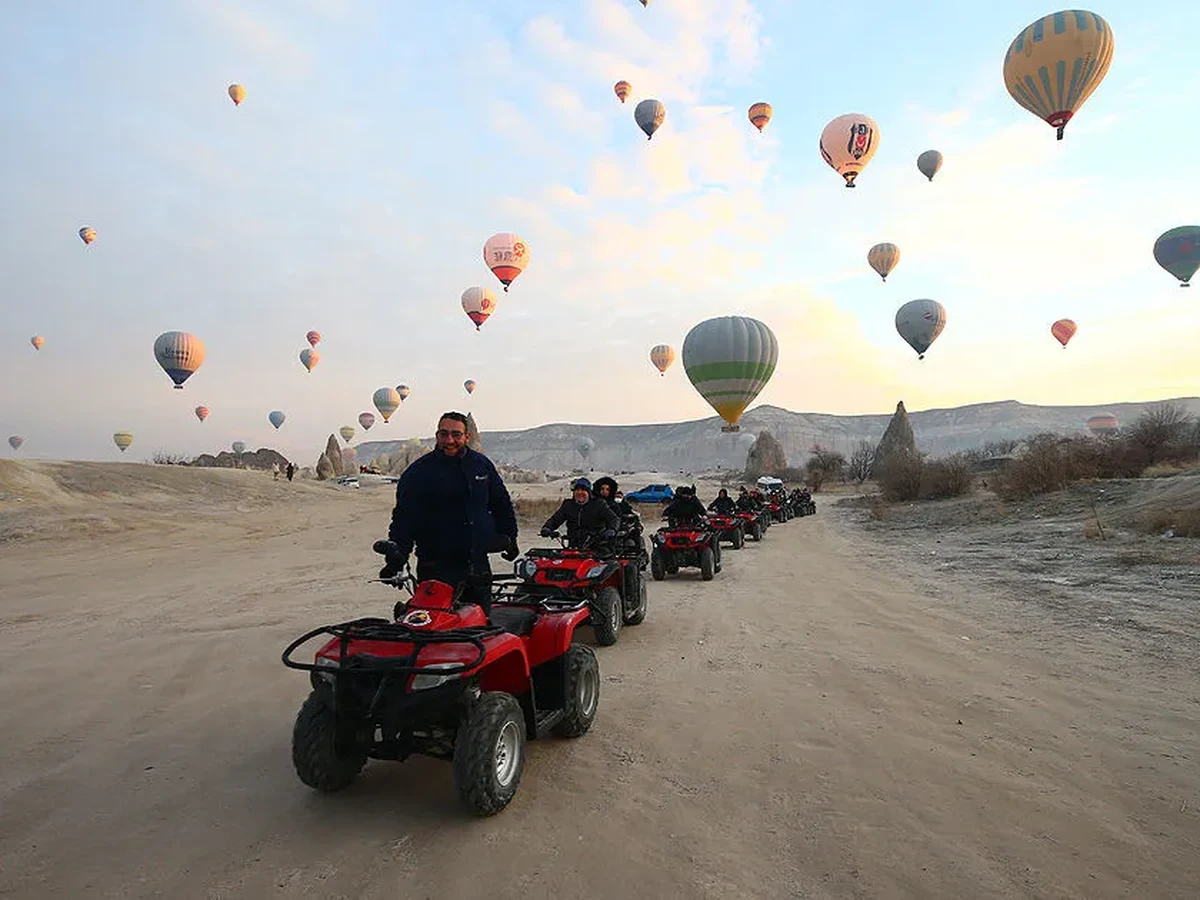 Guests riding ATVs through Cappadocia beneath hot air balloons at sunrise
