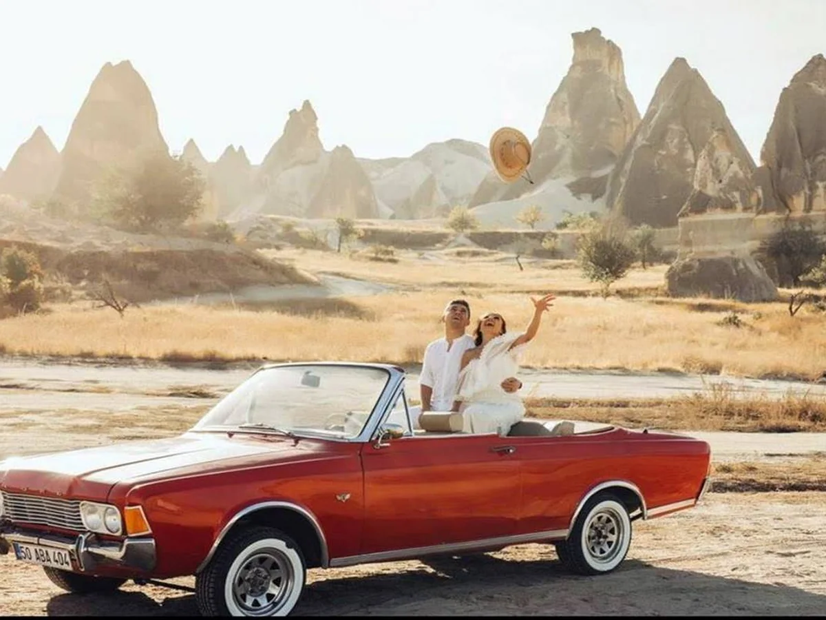 Couple waving from a red vintage convertible in Cappadocia